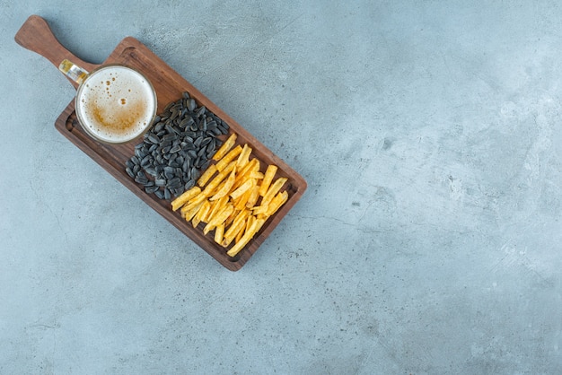 Patatas fritas, pipas de girasol y un vaso de cerveza en un tablero, sobre la mesa azul.