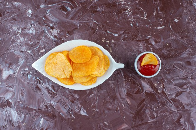 Patatas fritas en un plato junto a la salsa de tomate en un bol, sobre la mesa de mármol.