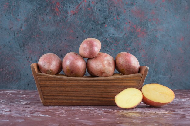 Patatas maduras en una caja de madera, sobre el fondo de mármol.