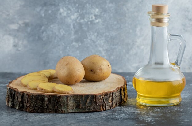 Patatas en rodajas y enteras sobre tabla de madera con aceite.