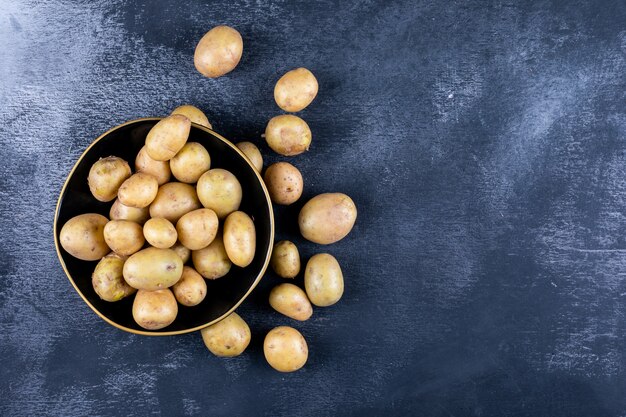 Patatas en un tazón y alrededor, sobre una mesa oscura