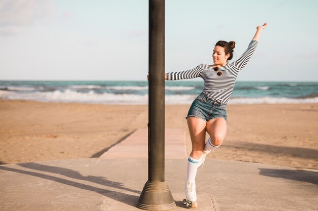 Patinador femenino joven de moda que sostiene el pilar que baila en la playa