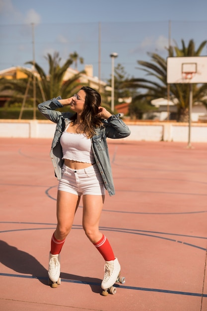 Foto gratuita patinador femenino joven sonriente que balancea en la cancha de básquet