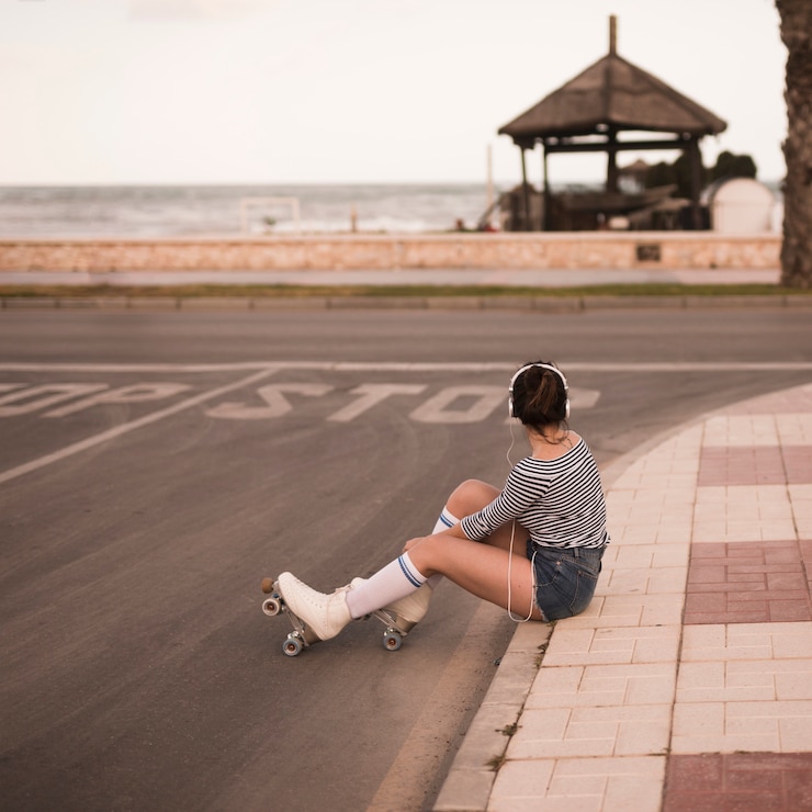 Foto gratuito patinador de sexo femenino joven que se sienta en música que escucha de la acera en el auricular que mira lejos