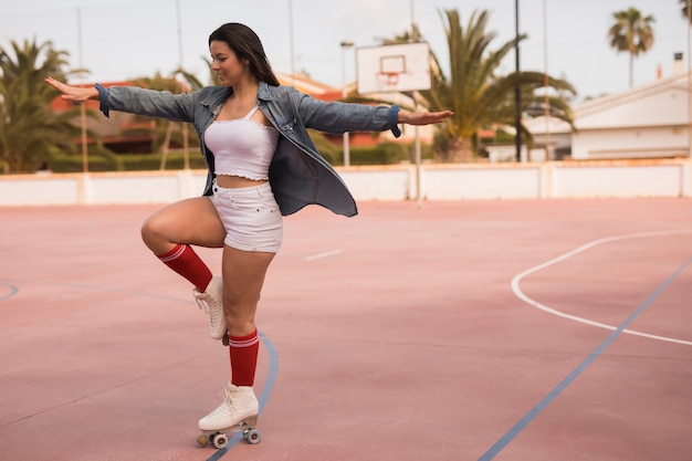 El patinador de sexo femenino sonriente que se coloca en una pierna outstretch sus manos