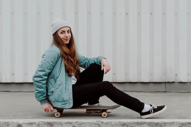 Patinadora sentada junto a su patineta al aire libre