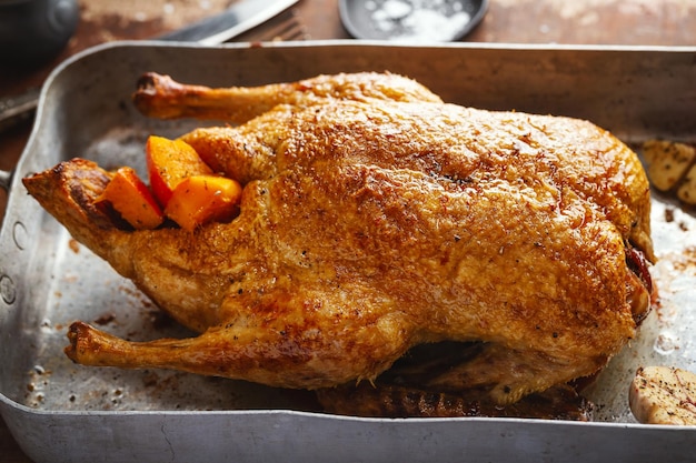 Pato asado al horno con verduras en sartén sobre fondo de madera vieja. De cerca