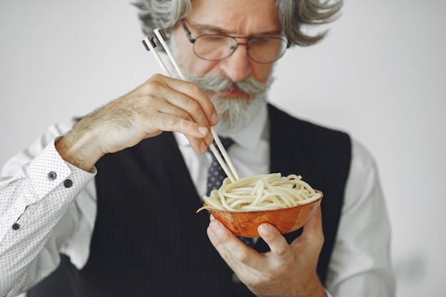 Pausa para almorzar. Hombre elegante en la oficina. Hombre de negocios con camisa blanca. El hombre come fideos.