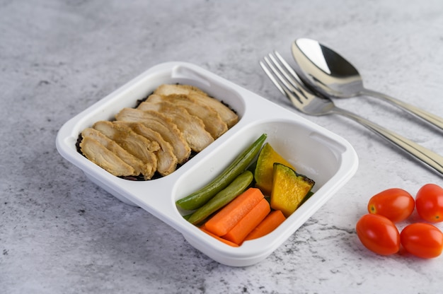 Pechuga de pollo al vapor en una caja de plástico con calabaza, zanahorias, frijoles eclosionados y tomate.