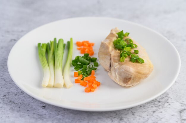 Pechuga de pollo al vapor en un plato blanco con cebolletas y zanahorias picadas
