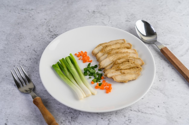 Foto gratuita pechuga de pollo al vapor en un plato blanco con cebolletas y zanahorias picadas