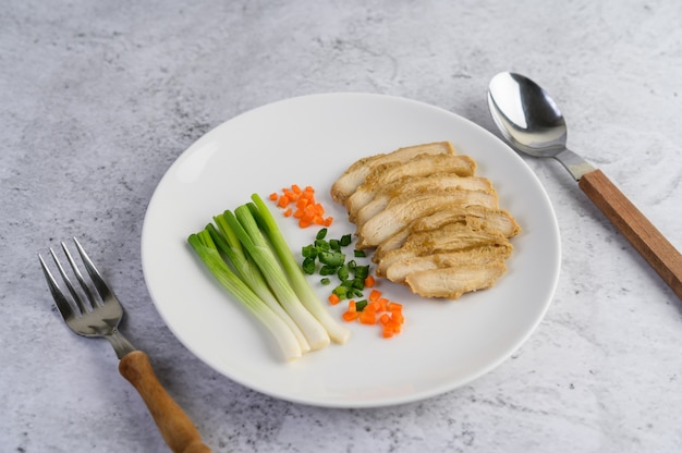 Pechuga de pollo al vapor en un plato blanco con cebolletas y zanahorias picadas
