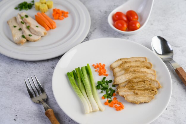 Pechuga de pollo al vapor en un plato blanco con cebolletas y zanahorias picadas