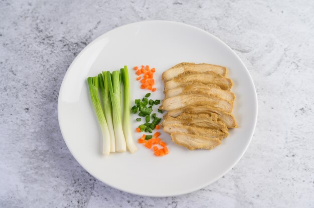 Pechuga de pollo al vapor en un plato blanco con cebolletas y zanahorias picadas