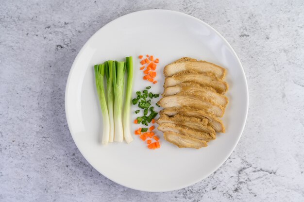 Pechuga de pollo al vapor en un plato blanco con cebolletas y zanahorias picadas