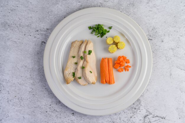 Pechuga de pollo al vapor en un plato blanco con cebolletas y zanahorias picadas