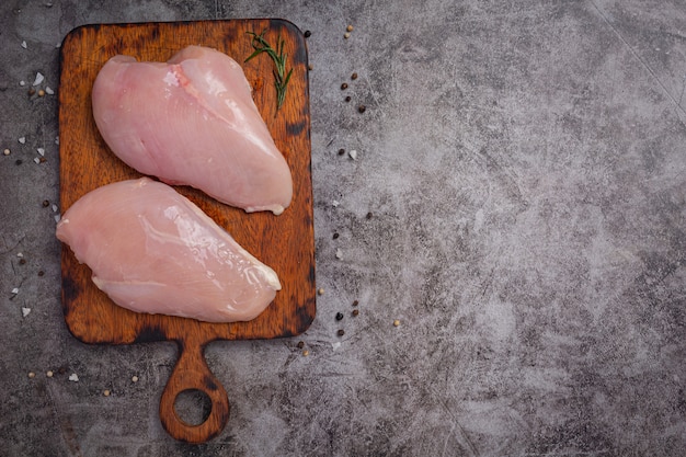 Foto gratuita pechuga de pollo cruda sobre la superficie oscura.