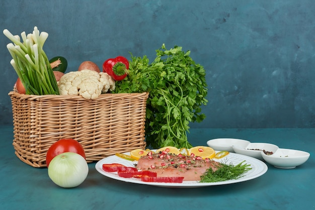 Pechuga de pollo con especias en un plato blanco con verduras alrededor.