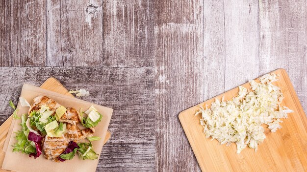 Pechuga de pollo a la parrilla en ensalada recién cortada junto a ensalada de repollo sobre tabla de madera