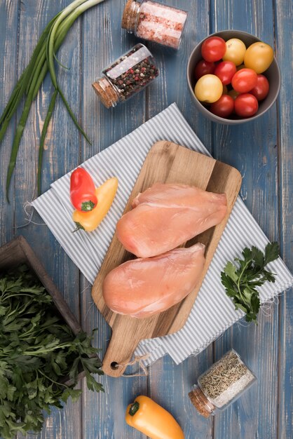 Pechuga de pollo plana sobre tabla de madera con pimientos y tomates