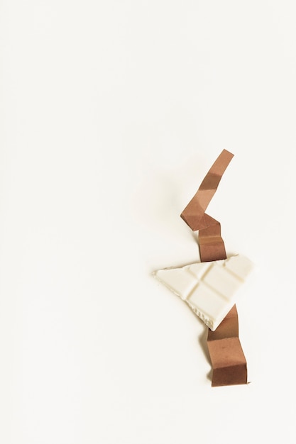 Pedazo blanco del chocolate en el papel marrón doblado de la tarjeta contra el fondo blanco