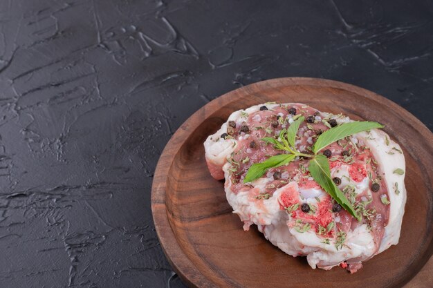 Pedazo de carne cruda en placa de madera decorada con menta fresca sobre fondo oscuro.