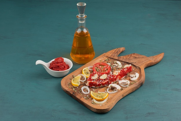 Pedazo de carne cruda con verduras en el cuadro azul junto a aceite y pasta de tomate.