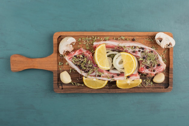 Pedazo de carne cruda con verduras sobre tabla de madera.