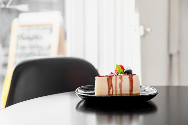 Pedazo de cheesecake de arándanos en un plato negro sobre la mesa de madera