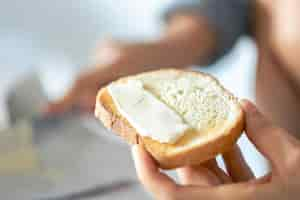 Foto gratuita un pedazo de pan con mantequilla en la mano de una mujer