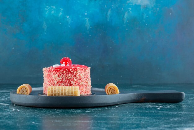 Pedazo de pastel de fresa y rollos de gofres sobre tabla de cortar negra.