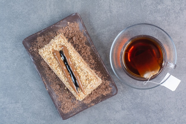 Un pedazo de pastel con una taza de café aromático en la mesa gris.