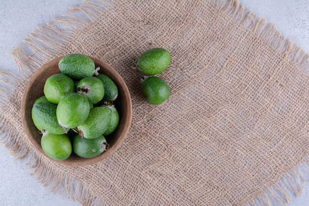 Pedazo de tela debajo de un cuenco pequeño de feijoas sobre fondo de mármol. Foto de alta calidad