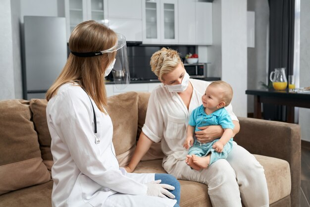 Pediatra en máscara médica visitando al bebé en casa
