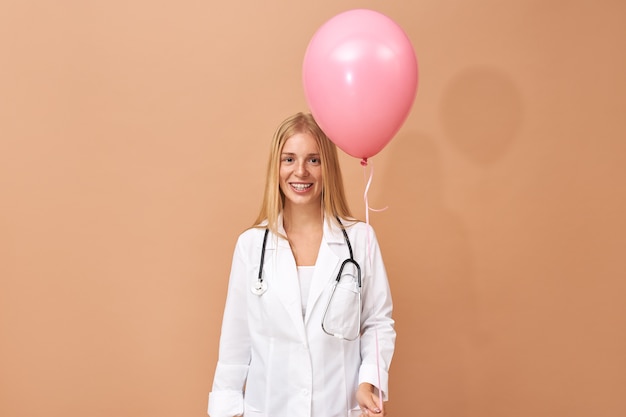 Foto gratuita pediatra mujer joven feliz emocional en bata quirúrgica divirtiéndose riendo con los ojos cerrados felicitando a su pequeño paciente enfermo en cumpleaños en el hospital