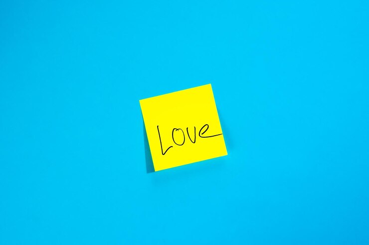 Foto gratuito pegatina amarilla con la inscripción amor en una vista superior de fondo azul