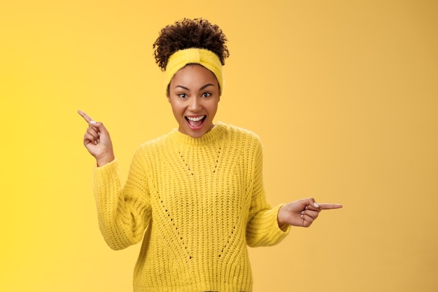 Peinado afro de mujer afroamericana carismática activa enérgica en diadema de suéter gritando fascinado entusiasta apuntando de izquierda a derecha impresionado variaty opciones increíbles, recogiendo productos.