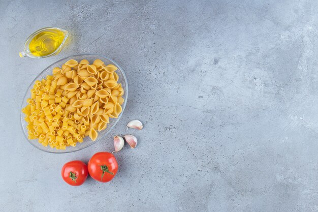 Pele la pasta cruda con Ditali Rigati seco y crudo en un recipiente de vidrio con tomates rojos frescos y ajo.