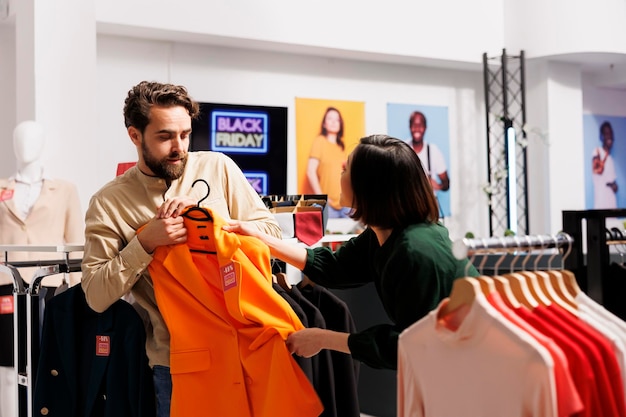 Pelea del Viernes Negro. La gente y los compradores pelean por la ropa durante las grandes ventas en el centro comercial, clientes hombres y mujeres enojados tirando de artículos de ropa y discutiendo mientras compran en la tienda durante los descuentos estacionales