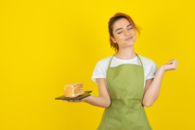 Pelirroja joven alegre con una rebanada de pastel fresco en la pared amarilla