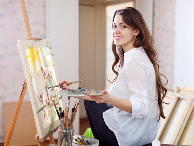 Pelo largo femenino artista pinta cuadro sobre lienzo