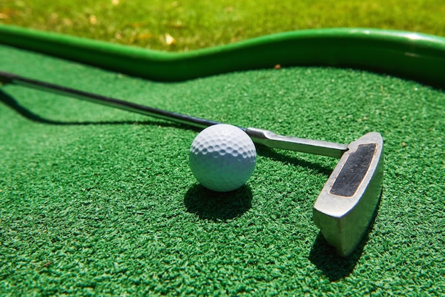 Pelota de golf y club de golf sobre césped artificial.