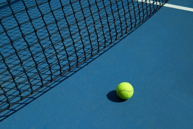 La pelota de tenis amarilla está tendida cerca de la red negra de la cancha de tenis abierta.