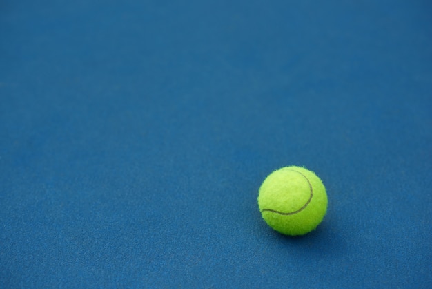 La pelota de tenis brillante amarilla está mintiendo en fondo azul de la alfombra. Hecho para jugar tenis. Cancha de tenis azul.