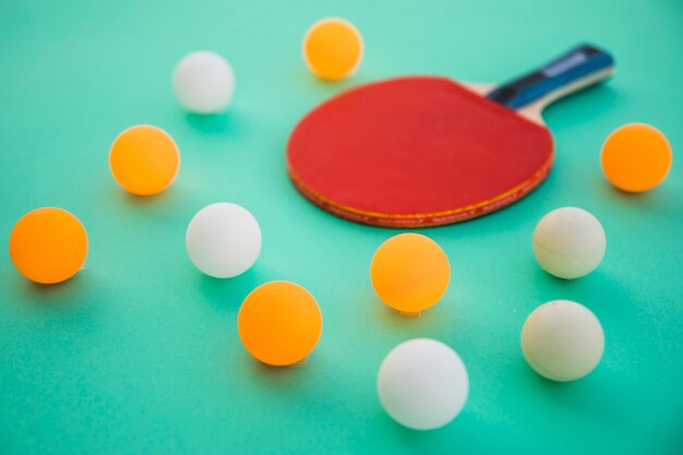 Pelotas de ping pong y raqueta de madera sobre fondo turquesa.