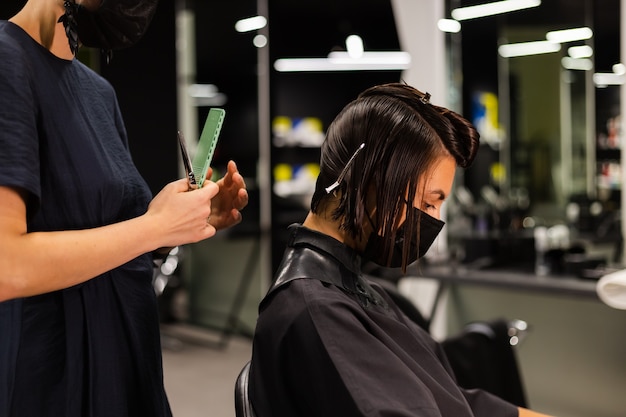 Una peluquera profesional hace el corte de pelo de un cliente. La niña está sentada en una máscara en el salón de belleza.