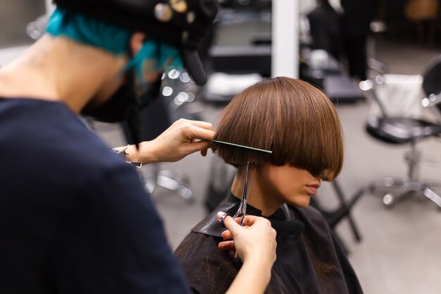 Una peluquera profesional hace el corte de pelo de un cliente. La niña está sentada en una máscara en el salón de belleza.