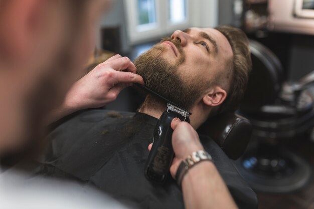 Peluquería anónima recortando la barba del hombre