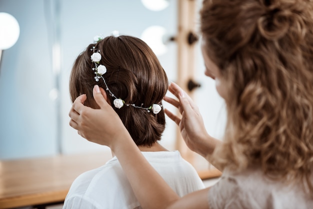 Peluquería femenina haciendo peinado a mujer morena en salón de belleza