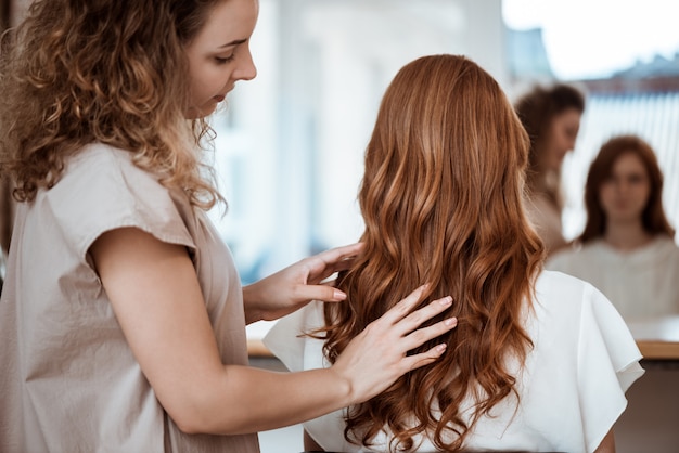 Peluquería femenina haciendo peinado a mujer pelirroja en salón de belleza